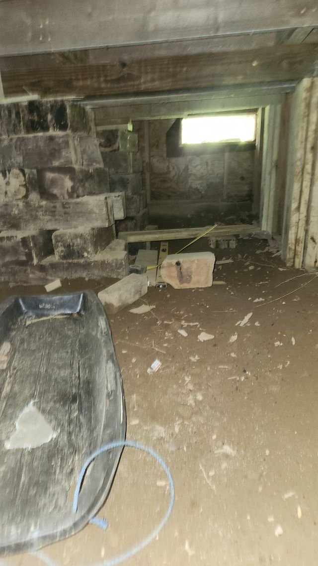 A black plastic sled on a flat dirt floor under the house